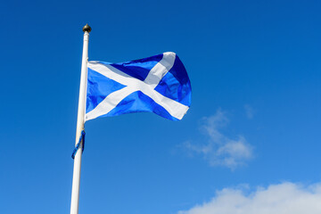 Flag of Scotland (Saltire or the Saint Andrew's Cross) blowing in the wind towards clear blue sky in a sunny summer day.