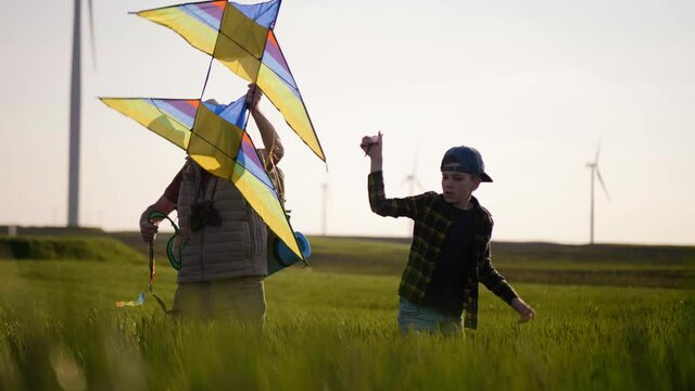 Grandfather and grandson release a flying kite on a windy field with windmills