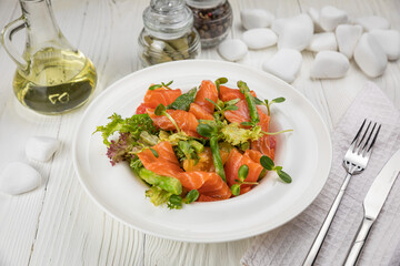 Salmon, asparagus and greens salad. On a white plate and white table.
