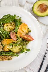 Grilled chicken salad, tomatoes, potatoes and greens. On a white plate and white table.
