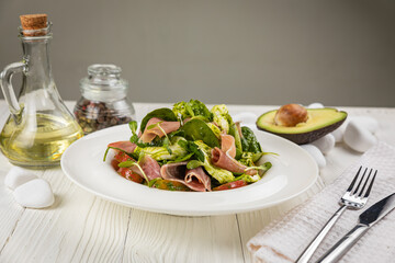 Salad with parma, mozzarella, tomatoes and greens. On a white plate and white table.

