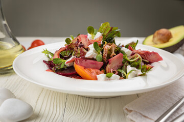 Salad of veal, goat cheese, greens. On a white plate and white table.
