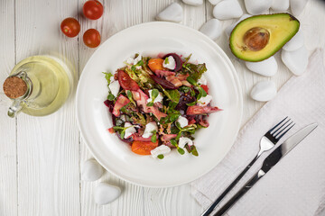 Salad of veal, goat cheese, greens. On a white plate and white table.
