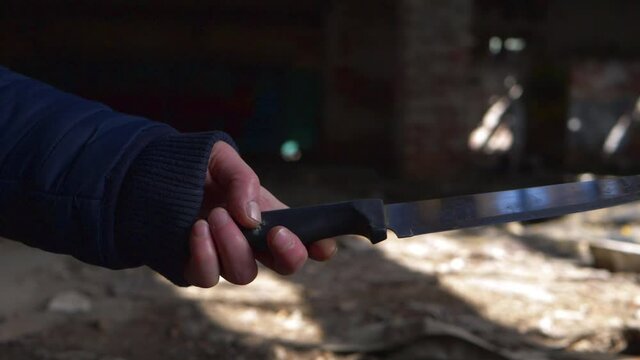 Criminal plays with knife in the shadows of derelict building 