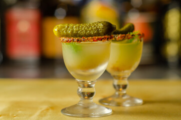Shaken vodka and pickle juice with ice in shot glass and garnishing with small pickled cucumber and dill