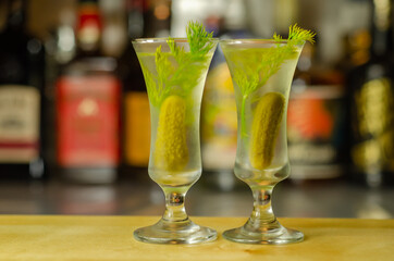 Shaken vodka and pickle juice with ice in shot glass and garnishing with small pickled cucumber and dill