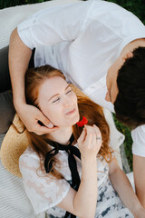 Young girl eating fresh sweet strawberry on a picnic is resting lying on her partner. Close-up of a happy woman having breakfast in nature.