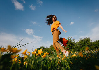 A young slender girl with curly hair developing in the wind runs in a meadow with yellow field dandelions in the park. Allergy free concept.