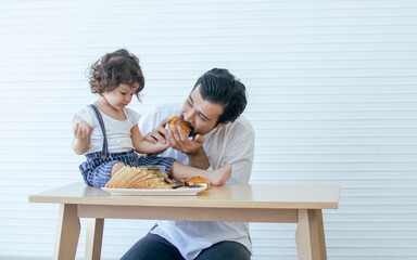 Caucasian handsome beard father or dad eating cookies and bread on the table at home together with his little adorable little girl. Copy space for advertisement. Education, Family and Kid Concept.
