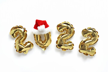 Christmas or New Year background. 2022 year, of golden balloons, on a white background, wearing a Santa Claus hat. Postcard or calendar. Happy New Year or Christmas.