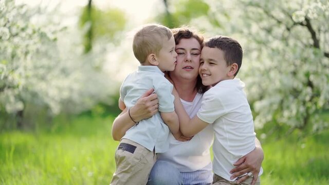 mother with sons kissing and cuddling in flowering garden. mother's day
