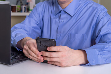 A man in a blue shirt looks at the phone, sitting at the table.