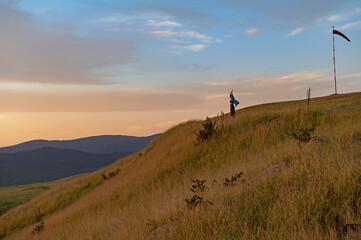 happy .young tourist woman with flying hair at panoramic view on high mountain at sunset. A borometer is behind her.