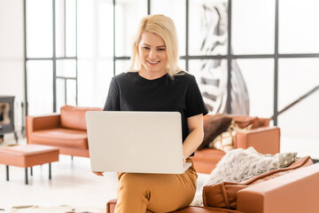 Happy casual beautiful woman working on a laptop sitting in the house.