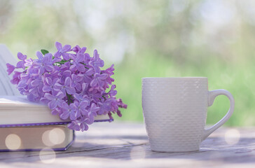 a branch of blooming lilacs on an open book and a white cup on a table in the garden