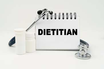 On a white table lies a stethoscope, pills and a notebook with the inscription - DIETITIAN