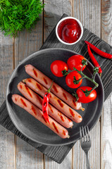 Grilled sausages with chili sauce and chili pepper on a light wooden background and cherry tomatoes