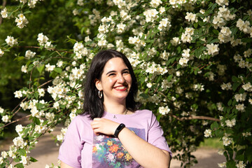 Photo of an attractive woman with black hair in the middle of nature during spring time, walking around and smiling during a sunny day