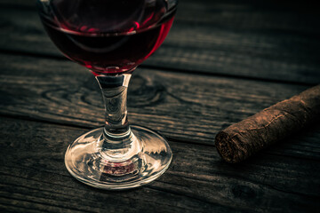 Glass of red wine and cuban cigar on an old wooden table. Close up view