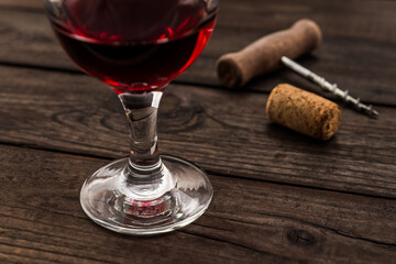 Glass of red wine and corkscrew with cork on an old wooden table. Close up view, focus on the glass of red wine