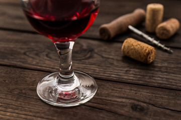 Glass of red wine and corkscrew with corks on an old wooden table. Close up view, focus on the glass of red wine