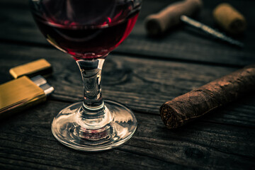 Glass of red wine and cuban cigar with corkscrew and corks on an old wooden table. Close up view, focus on the cuban cigar