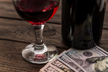 Bottle of red wine with a glass of red wine and money on an old wooden table. Close up view, focus on the glass of red wine