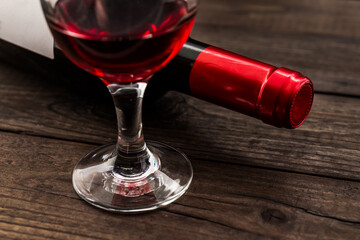 Bottle of red wine with a glass of red wine on an old wooden table. Close up view, focus on the glass of red wine