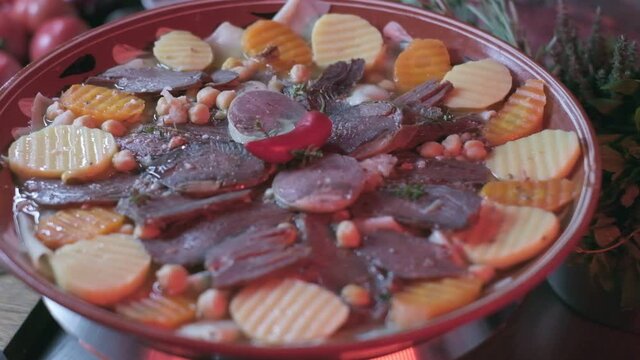 Close-up of national Kazakh dish Beshbarmak made of veggies, dough and horsemeat served in deep clay dish with hot red pepper on top