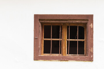 Window with a wooden frame on a white wall of the house. There is a grille in the windows. There are cobwebs around the window.