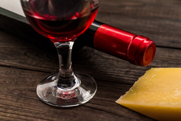 Bottle of red wine with a glass of red wine and a pice of parmesan on an old wooden table. Close up view