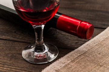 Bottle of red wine with a glass of red wine and piece of canvas on an old wooden table. Close up view, focus on the glass of red wine