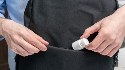 Man puts container of pill in a backpack, male hands, cropped image, close-up