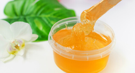 Sugar paste or wax honey in a transparent jar and white orchid on a white background. Sugaring. Depilation and beauty concept.