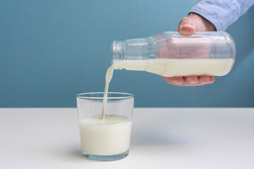 Man pouring milk in a glass, man's hand, blue background, cropped image, close-up, copy space - Powered by Adobe