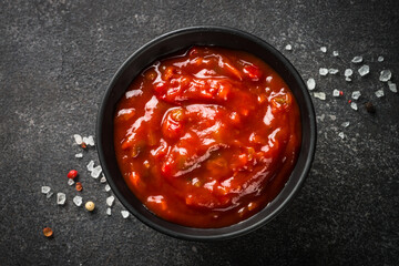 Tomato sauce in a bowl at black stone table. Top view image.