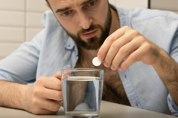 Hangover man has a headache, pain pills and a glass of water, close-up, cropped image