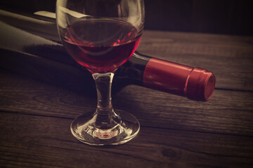 Bottle of red wine with a glass of red wine on an old wooden table. Angle view, focus on the glass of red wine