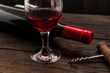 Bottle of red wine with a glass of red wine and corkscrew on an old wooden table. Angle view, focus on the glass of red wine