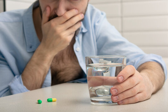 Sick person has a headache, pain pills and a glass of water, close-up, cropped image