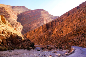 View on empty curved road through narrow dry limestone canyon from shade to sunshine - todra (todgha) gorge, morrocco - obrazy, fototapety, plakaty