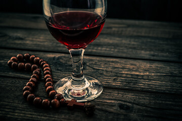 Glass of red wine and rosary on an old wooden table. Angle view, focus on the glass of red wine
