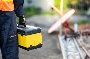 Male maintenance worker hand carrying yellow work tool box at construction site. Equipment for...