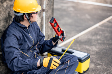 Maintenance worker man or male Asian mechanic wearing protective suit and helmet holding tape measure and level tool at construction site. Equipment for civil engineering project