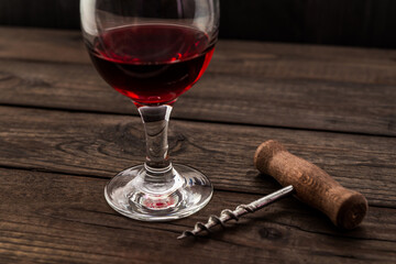 Glass of red wine and corkscrew on an old wooden table. Angle view