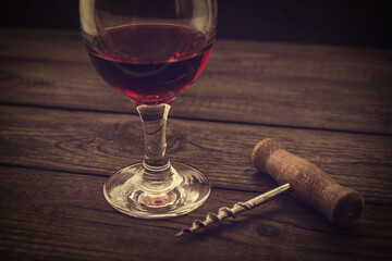 Glass of red wine and corkscrew on an old wooden table. Angle view