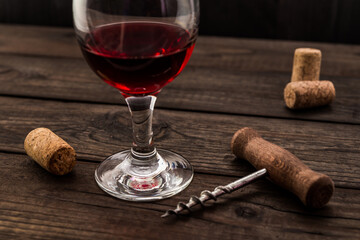 Glass of red wine and corkscrew with corks on an old wooden table. Angle view