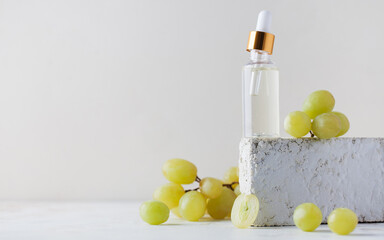Grape cosmetics. Glass bottle with skin care product with grape extract on a pedestal. Copy space.
