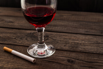 Glass of red wine and cigarette on an old wooden table. Angle view, focus on the glass of red wine