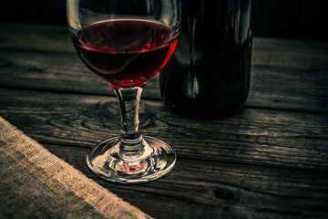 Glass of red wine with bottle of red wine and piece of canvas on an old wooden table. Angle view, focus on the glass of red wine